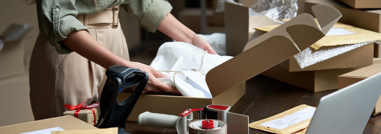 Closeup view of female online store small business owner seller entrepreneur packing package post shipping box preparing delivery parcel on table. Ecommerce dropshipping shipment service concept.